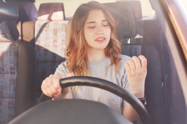 Verveeld mooie jonge dame kijkt naar haar manicure terwijl staat in de file bij de auto, ervaren ervaren bestuurder