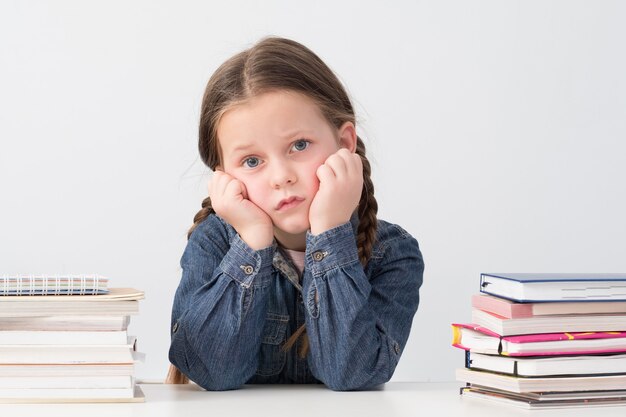 Verveeld schoolmeisje zitten met hoofd rustend op handen, stapels boeken rond.