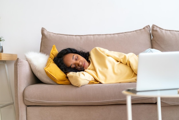 Verveelde Afro-Amerikaanse vrouw die op de bank in de woonkamer slaapt terwijl de film wordt afgespeeld op de laptop