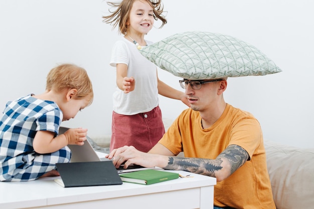 Verveelde kinderen knoeien met hun vader die op zijn laptop werkt