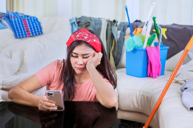 Verveelde meid die een mobiele telefoon gebruikt in een rommelige woonkamer