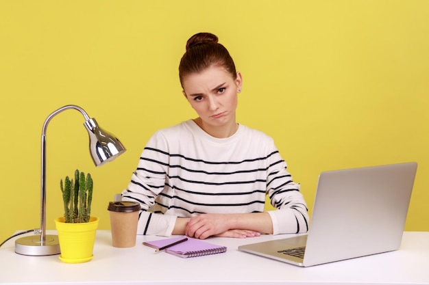 Verveelde ongelukkige vrouw officemanager met gestreept shirt zittend op de werkplek kijkend naar camera