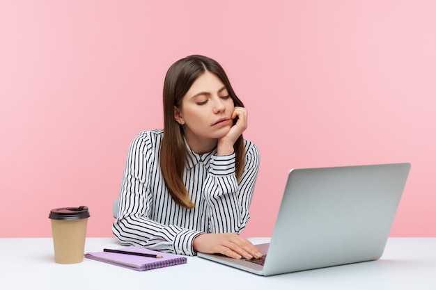 Verveelde ongelukkige zakenvrouw zittend op de werkplek kijkend naar laptopscherm met videogesprek, moe van online conferentie, uitstel. Indoor studio-opname geïsoleerd op roze background