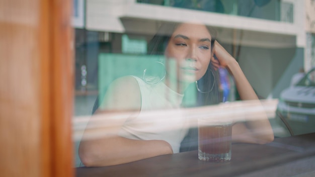 Verveelde vrouw zit in een café en kijkt door het raam op een stedelijke straat van dichtbij.