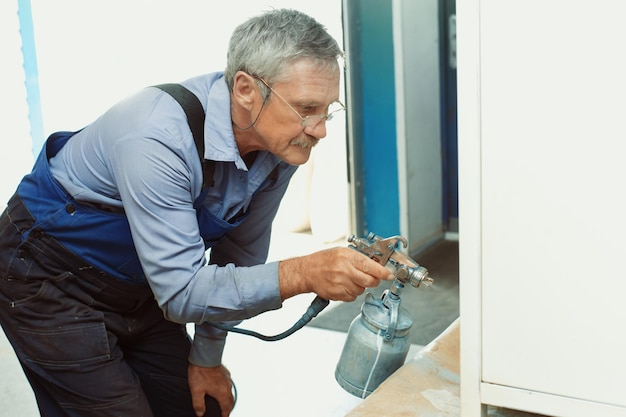 Verven van metalen producten Een oudere man schildert een kast met een compressor
