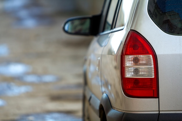 Vervoer, rijden en motorvoertuigconcept - close-up achteraanzicht detail van rode stoplichten en spiegel van nieuwe glanzende luxe zilveren auto op wazig kleurrijke scène.