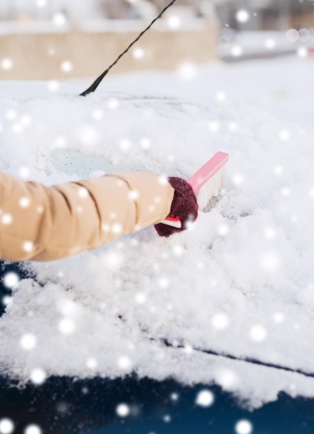 vervoer, winter, weer, mensen en voertuigconcept - close-up van vrouw die sneeuw van autovoorruit schoonmaakt met borstel