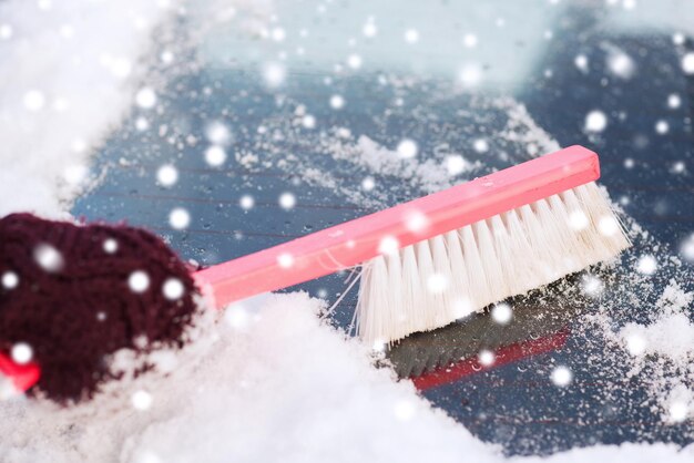 vervoer, winter, weer, mensen en voertuigconcept - close-up van vrouw die sneeuw van autovoorruit schoonmaakt met borstel