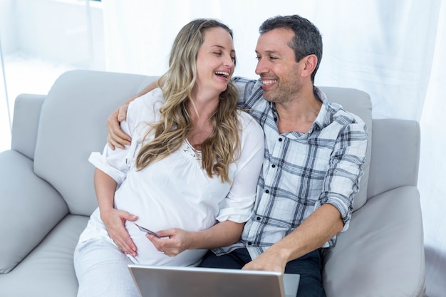 Verwacht paar zittend op een sofa en met behulp van laptop