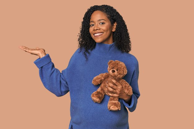 Verwachtende Afro-Amerikaan met een teddybeer die een kopieringsruimte op een handpalm toont