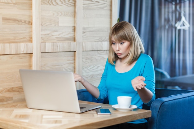 Verward onzekere jonge vrouw die aan de laptop werkt schouders opzuigen ziet er twijfelachtig en verbijsterd uit