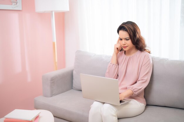 Verwarde Aziatische vrouw bij het gebruik van laptop op de bank thuis