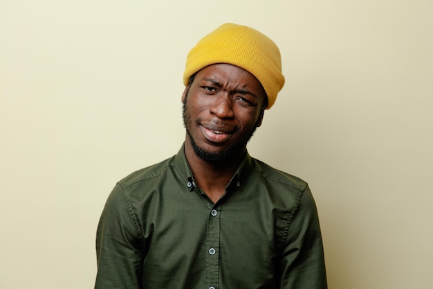 Verwarde jonge Afro-Amerikaanse man in hoed met groen shirt geïsoleerd op een witte achtergrond