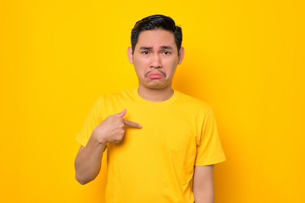 Verwarde jonge Aziatische man in casual t-shirt wijzend op zijn borst, zich verbaasd voelend over iets geïsoleerd op gele achtergrond Mensen lifestyle concept