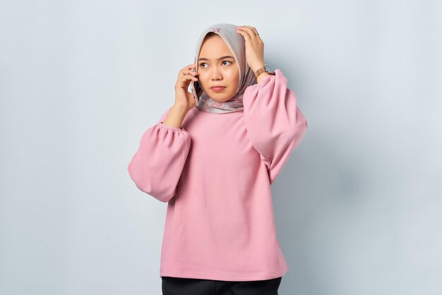 Verwarde jonge Aziatische vrouw in roze shirt praten op mobiele telefoon geïsoleerd op witte achtergrond