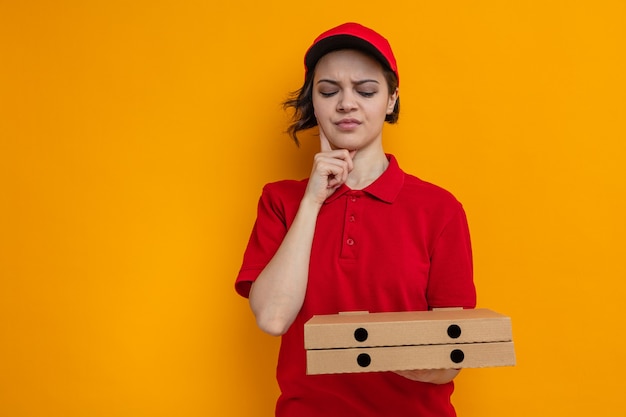 Verwarde jonge mooie bezorger die pizzadozen vasthoudt en bekijkt