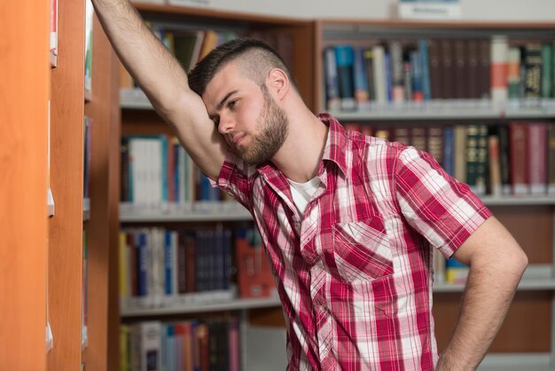 Verwarde mannelijke student die veel boeken leest voor examen