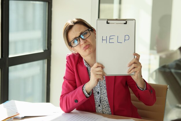 Verwarde vrouw die op kantoor zit, heeft een inscriptie die helpt bij overbelasting op het werk, veel werk