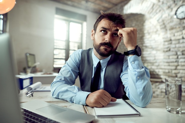 Verwarde zakenman die aan iets denkt terwijl hij aan zijn bureau op kantoor werkt