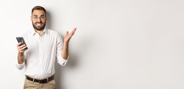 Verwarde zakenman die vreemd bericht op mobiele telefoon leest en er geïrriteerd uitziet terwijl hij over een witte achtergrond staat