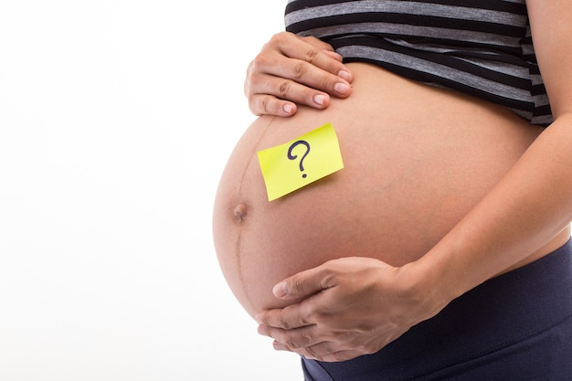 Verwarde zwangere vrouw met vraagtekens op papieren stickers op buik.
