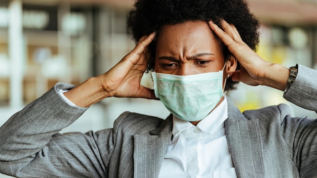 Verwarde zwarte zakenvrouw die een gezichtsmasker draagt terwijl ze zich gefrustreerd voelt tijdens een virusepidemie