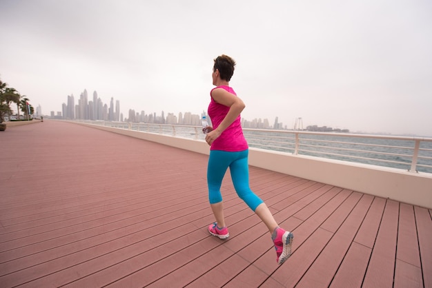 very active young beautiful woman busy running on the promenade along the ocean side with a big modern city in the background to keep up her fitness levels as much as possible