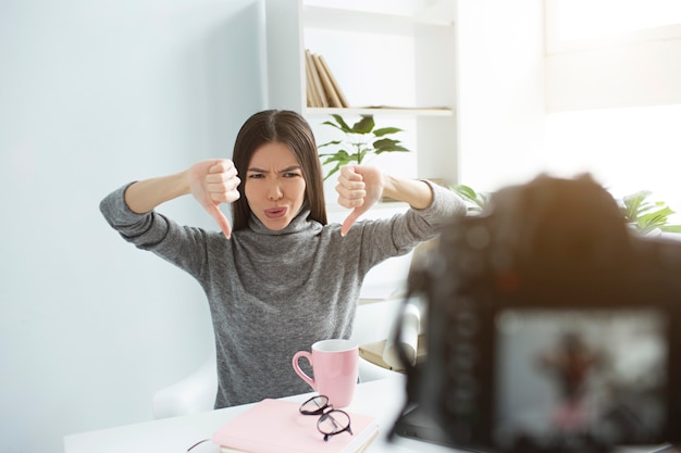 Very angry female person is looking to the camera and showing her thumbs down with both hands