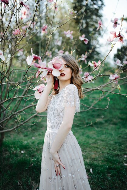 Very beautiful girl the bride under a veil, beige wedding dress near the tree Sakura is looking down, nature