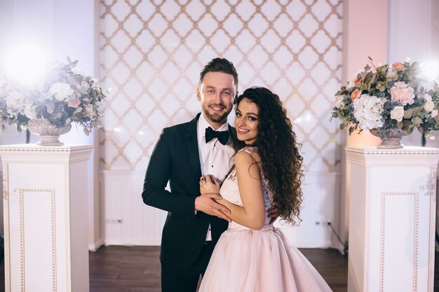 Sposi molto belli e felici stanno vicino a un arco di nozze splendidamente decorato durante la loro cerimonia di matrimonio