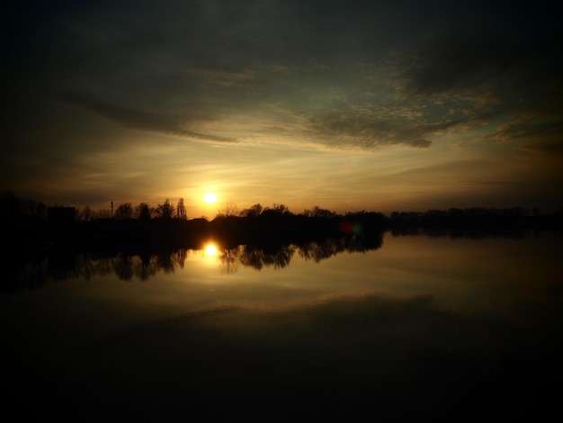 Very beautiful sunset over the water River bank and horizon Bright clouds are drawn by the evening sun Setting sun Yellow orange gray dramatic sky and clouds Night falls dusk comes