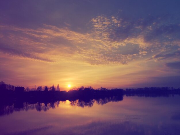 Very beautiful sunset over the water River bank and horizon Bright clouds are drawn by the evening sun Setting sun Yellow pink orange purple dramatic sky and clouds Night falls dusk comes