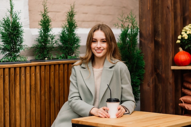 Very beautiful young woman, sit in Cafe and drink coffee or tea with croissant, street front view