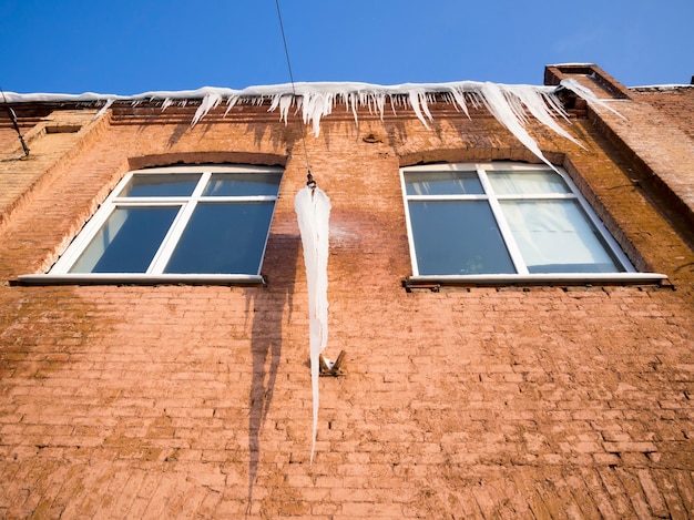 Very big icicle hanged on the wire close to old red brick wall