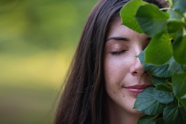 Foto molto ritratto del primo piano di una giovane donna lentigginosa che copre parte del viso con foglie di tiglio verde