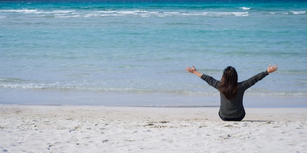 Foto donna molto felice sedersi sulla sabbia, guardare la splendida vista sul mare.