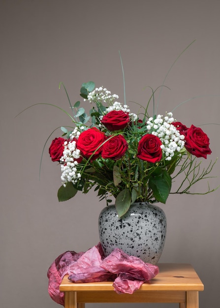 A very large bouquet of red roses with white flowers in a gray vase on a wooden t