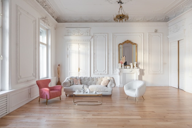 Very light baroque style luxury interior of big sitting room. White walls decorated with awesome stucco. Royal style apartment with chic furniture with gold elements