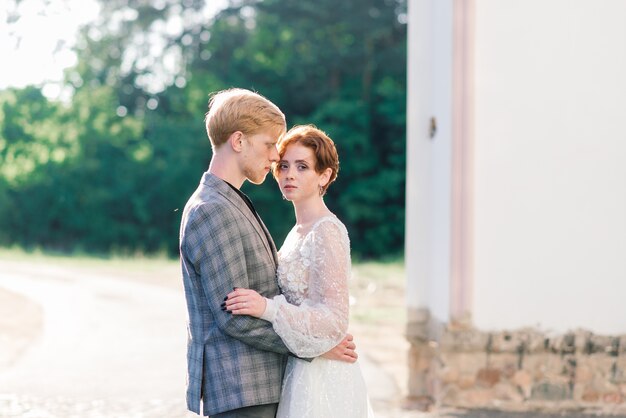 とても素敵な赤毛の若いちょうど結婚している幸せなカップルが屋外の夕日でキス