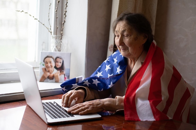 very old senior woman with laptop and usa flag.