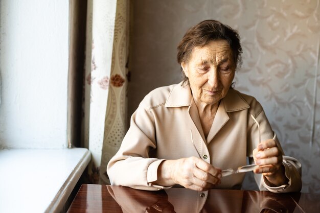 A very old woman puts on glasses and looking at the camera