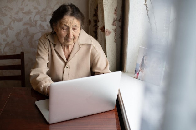 very old woman using laptop sitting at home.