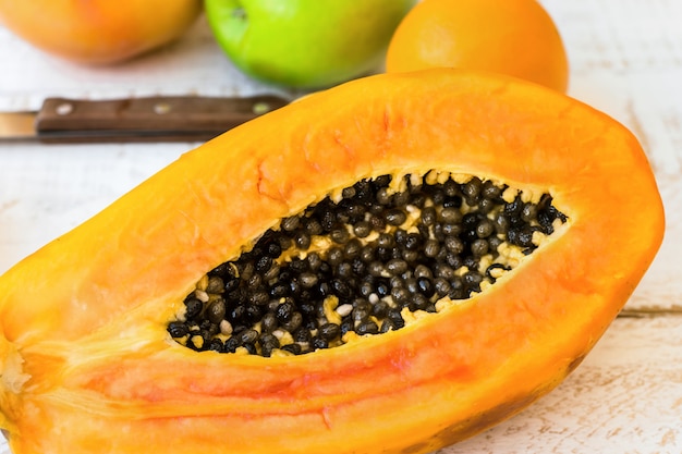 Very ripe juicy papaya cut in half on wood kitchen table with citrus fruits, apples, top view