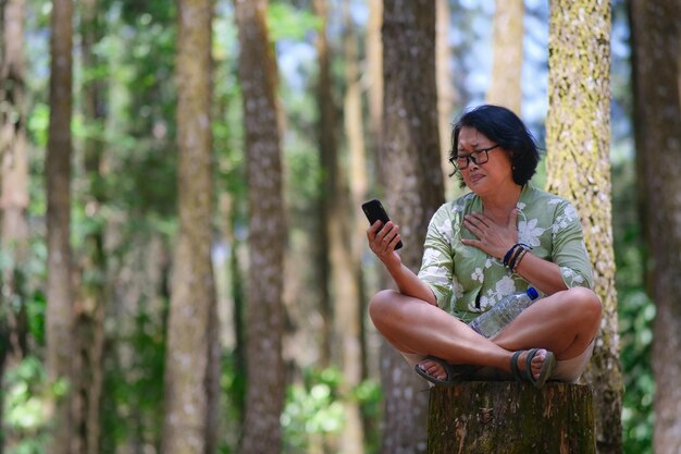 Photo very sad facial expression of a woman sitting in the park after reading messages on her smartphone