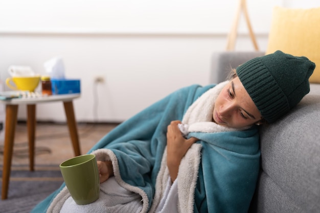 Photo very sick young woman sitting on the floor covered with a blanket