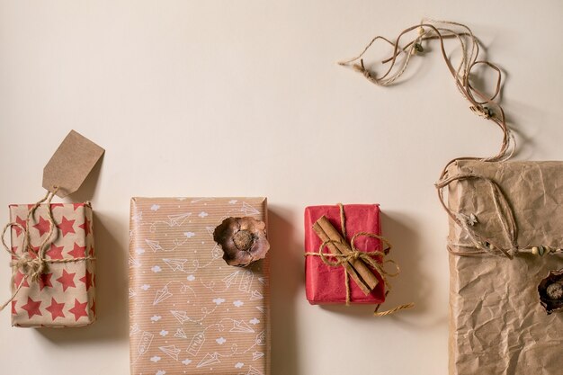 Verzameling kerstcadeaudozen in milieuvriendelijk ambachtelijk papier in rij versierd met kaneelstokjes op beige papieren achtergrond. Eco kerstcadeau concept. Plat leggen, ruimte kopiëren