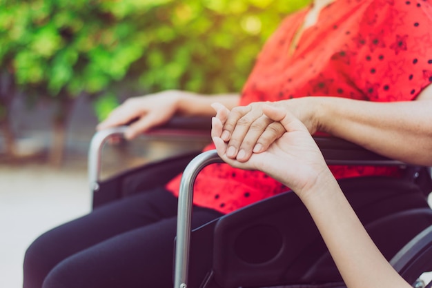 Verzorger hand vasthouden aan Aziatische oudere vrouw zittend op rolstoel, Senior verzekeringsconcept