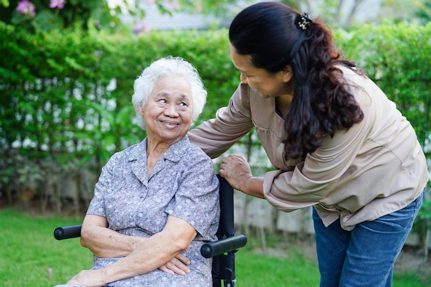 Verzorger helpt Aziatische bejaarde vrouw met een handicap die op een rolstoel zit in het medische concept van het park