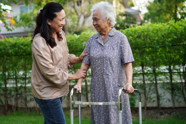 Verzorger helpt Aziatische bejaarde vrouw met een handicap die op een rolstoel zit in het medische concept van het park