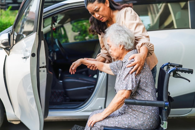 Verzorger helpt Aziatische bejaarde vrouw met een handicap om in haar auto medisch concept te komen